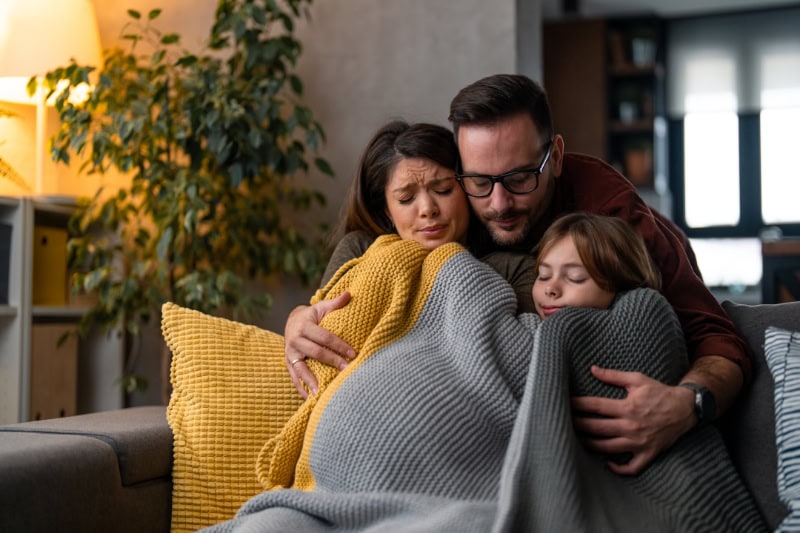 Why Isn’t My Furnace Heating My Entire Home? Photo of a family of three huddled under a blanket to keep warm.