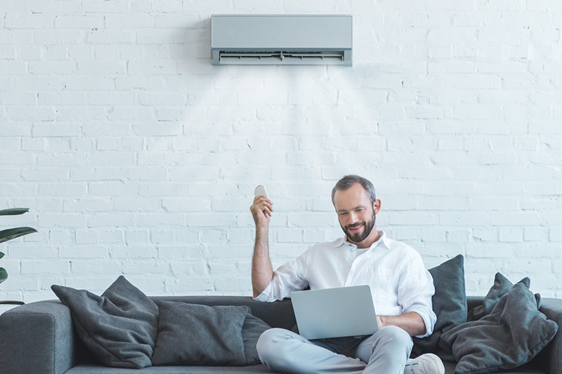 man effortlessly controlling Ductless unit with remote from his couch.